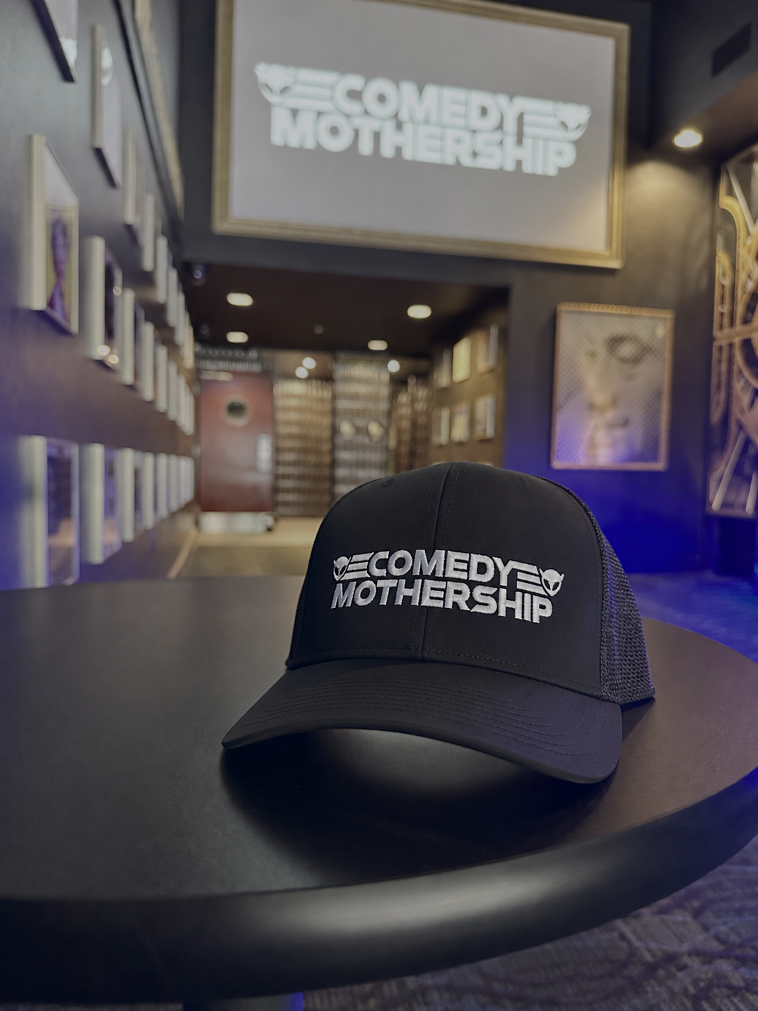 Comedy Mothership embroidered black trucker hat displayed inside the venue in Austin